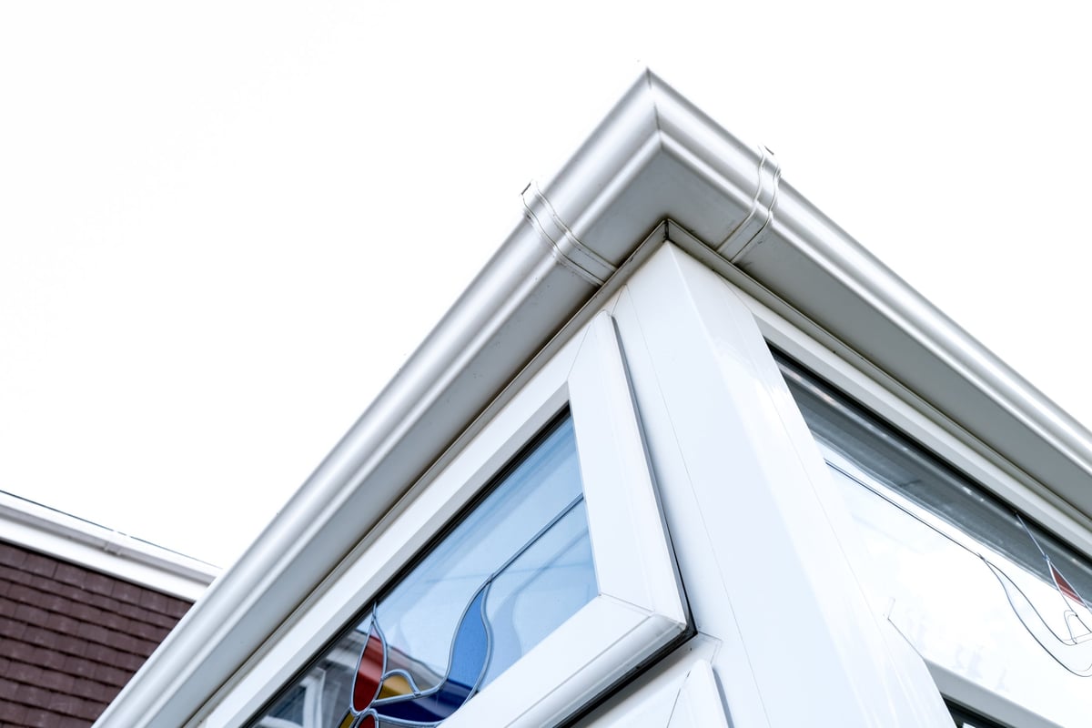 Large PVC conservatory with leaded light double glazed windows attached to a family home against a bright sky